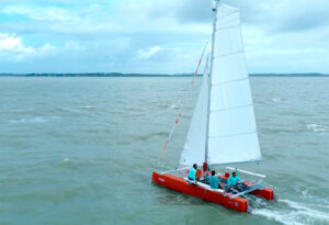 Catamarã à vela BV 21 da Bate Vento com casco vermelho navegando com tripulação durante testes no mar.